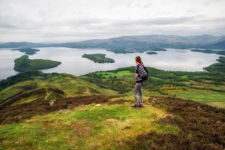 Woman standing on top of a grassy hill, looking out to smaller hills