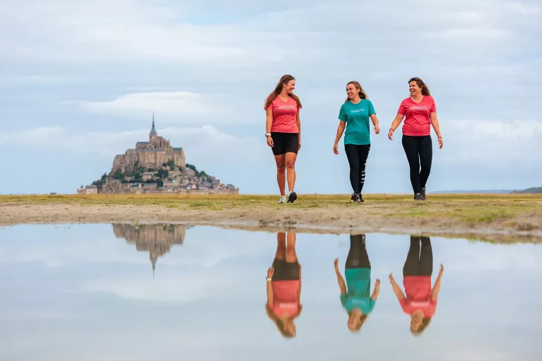 Three women walking on an empty valley, with a large castle in the distance