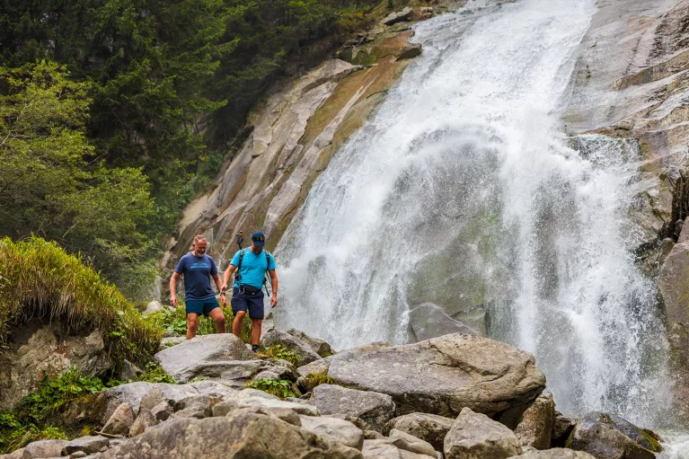 Two men hiking on a rocky trail next to a waterfall