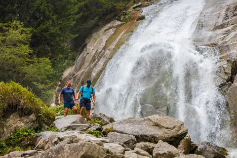 Two men hiking on a rocky trail next to a waterfall