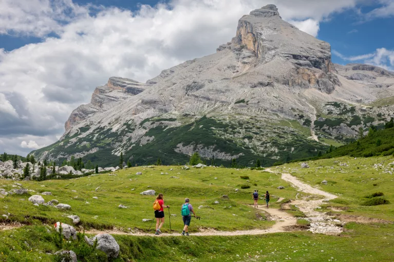Group of people hiking on a dirt trail, towards a large mountain