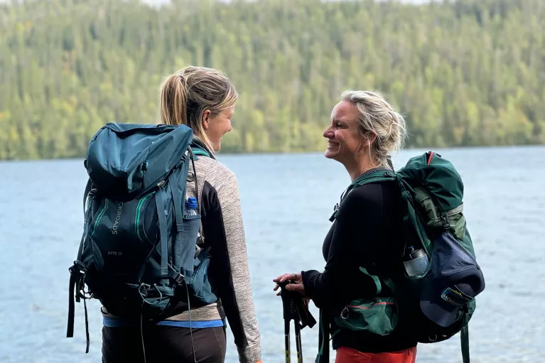 Two women smiling while standing in front of a lake