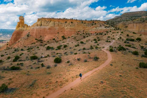 Top view of a man in blue ascending a dirt trail towards a mountain