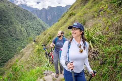 Woman and man walking on a dirt trail, smiling and looking out towards large hills