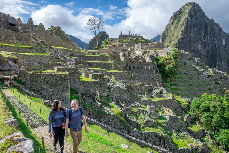 Man and woman smiling while walking on a stone path, with Machu Picchu in the background