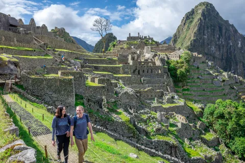 Man and woman smiling while walking on a stone path, with Machu Picchu in the background