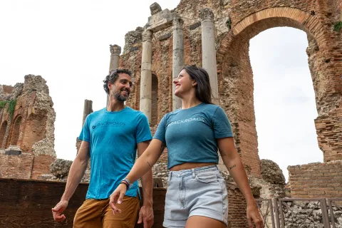Man and woman smiling while looking at each other, with a large stone arch in the background