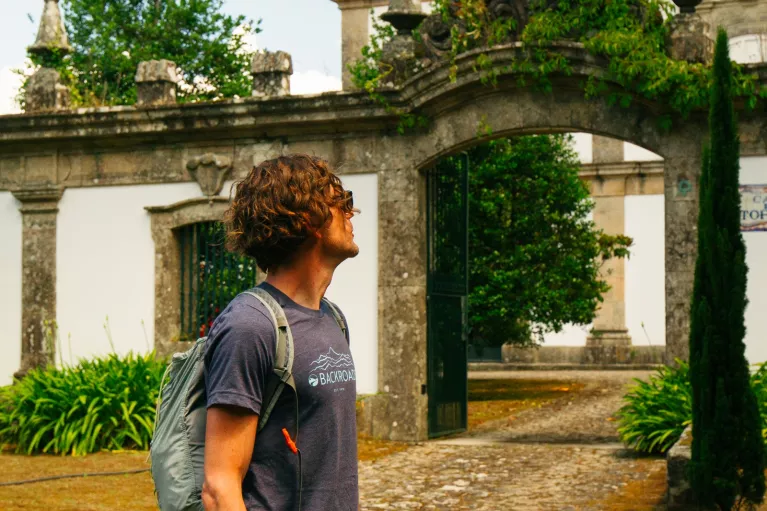 Man standing in front of a stone palace, surrounded by tall trees and bushes