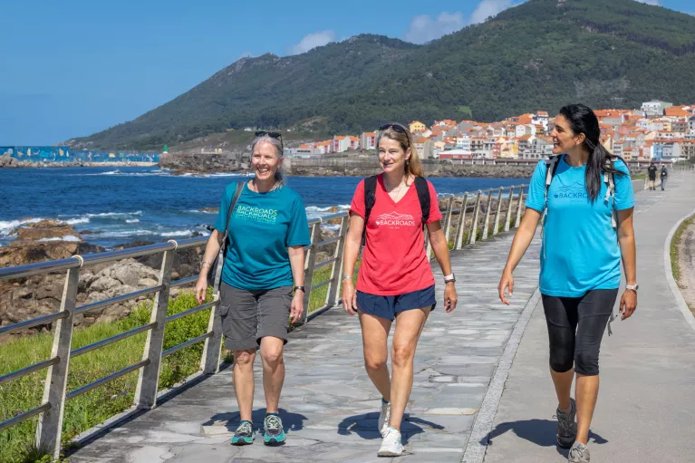 Three women walking on a stone path next to the ocean side