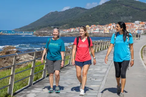 Three women walking on a stone path next to the ocean side