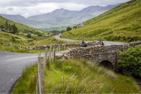 Hairpin road in the middle of a grassy valley, with two people biking on the road