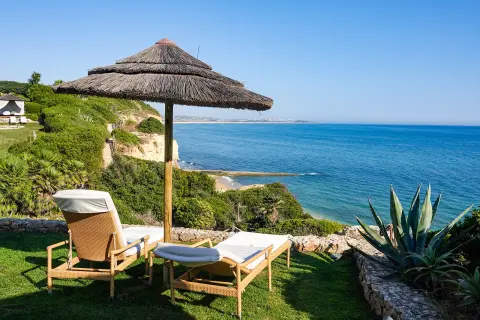 Two sun chairs below an umbrella on the coast of Portugal.