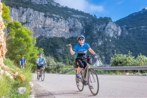 Group of people biking on a road with large mountains and cliffs in the background