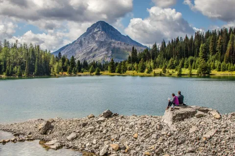 Man and woman sitting on a large boulder in front of a lake