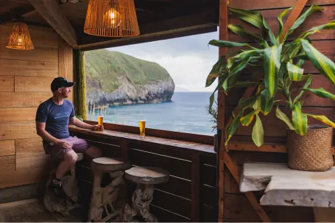 Man sitting on a stool, holding a beer and looking out towards the ocean