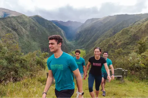 Group of people smiling while hiking up a grassy hill