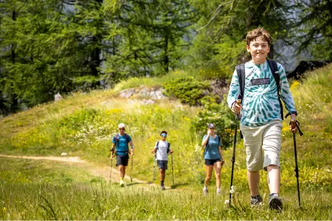 Family hiking on a trail in a valley, with a boy using hiking poles