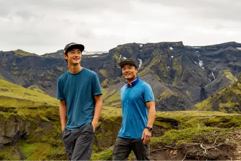 Two men smiling while walking in a valley with large mountains in the background