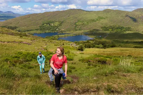 Two women ascending a grassy hill, with a lake in the distance
