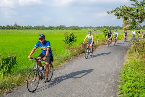 Group of people biking on a road next to a field of grass
