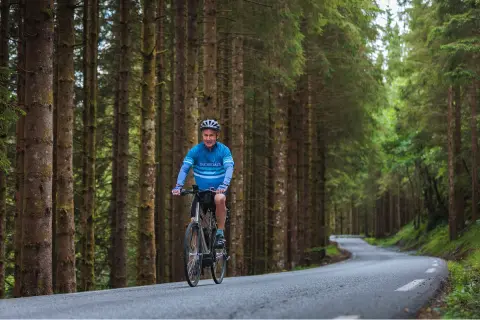 Man biking on an empty road in the middle of a forest