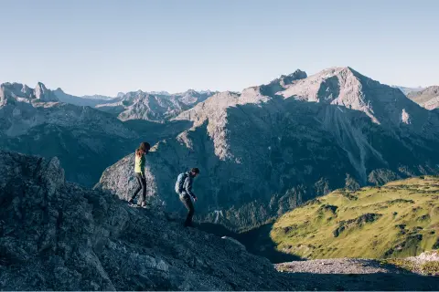 Two people descending down a mountain, with larger mountains in the distance