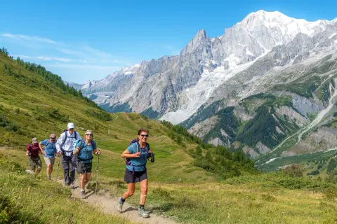 Group of people running on a grassy trail, with large mountains in the distance