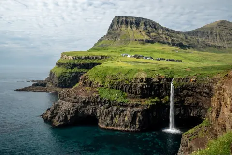 Large, grassy cliff with a waterfall and the ocean below