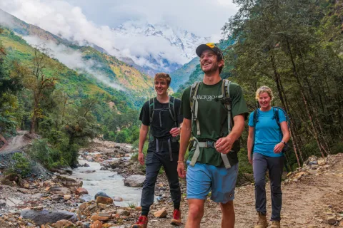 Two men and one woman walking along a frozen river with a forest in the background