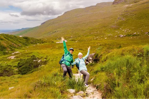 Man and woman smiling with their arms open, in the middle of a trail in the valley
