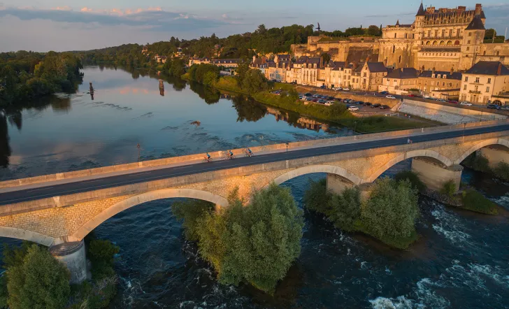 Bird's eye shot of cyclists over Loire River during sunset.  Château Royal d'Amboise behind.