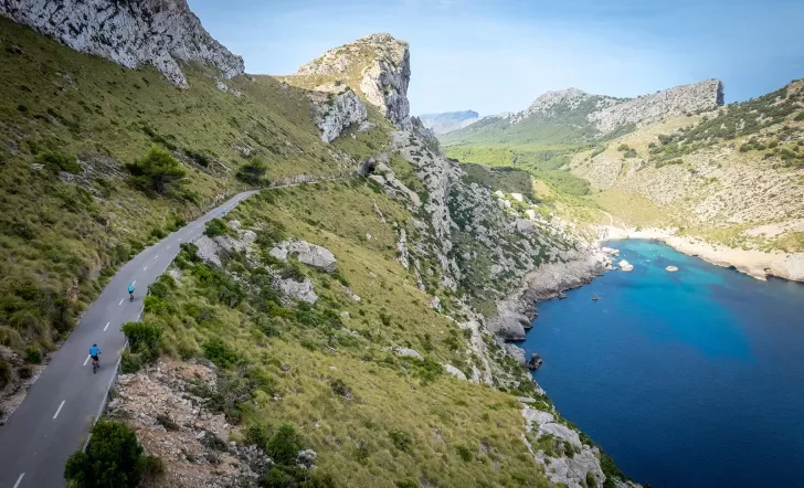 Two bikers riding around a bend on the coast of Mallorca.