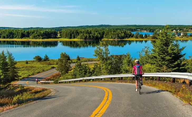 Guest cycling down road, large lake or river in background.