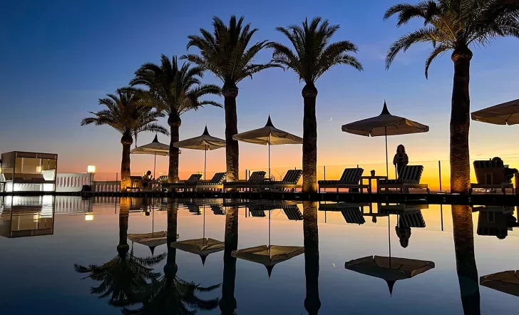 Sunset shot of still resort pool, palms, recliners.
