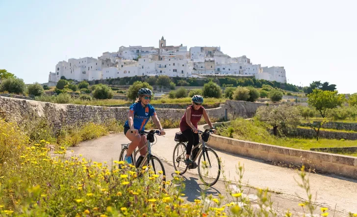 Two guests cycling in front of Ostuni hilltop.