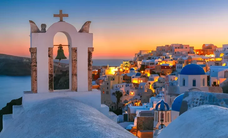 Sunset shot of Santorini, city lit up, church bell in foreground.