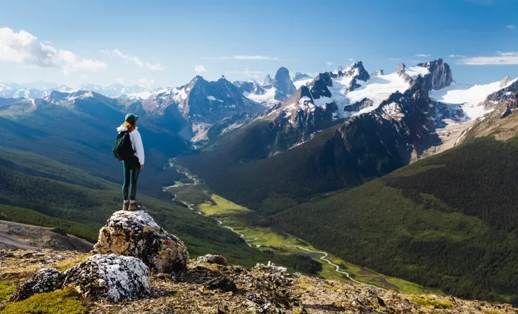 Guest standing on rocky hilltop, looking towards larger mountains.