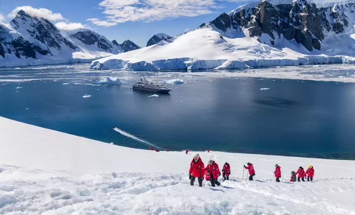 Hikers trekking up a snowy hill in Antarctica with a cruise ship anchored in the background