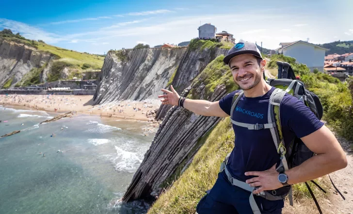 Leader gesturing to craggy cliffs, large beach, buildings dotting cliffside.