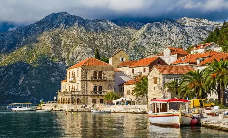 Shot of Croatian houses on coast, boats, mountain in distance.