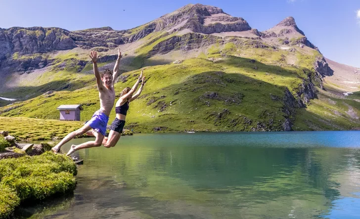 Two guests jumping into small lake, sharp cliffs and small shack in background.