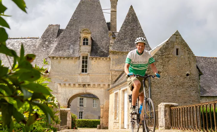Man smiling while riding a bike with a stone castle in the background