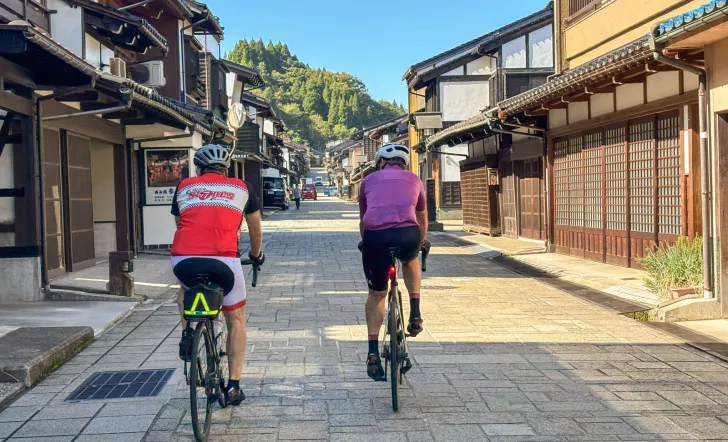 Two men biking on a stone road in the middle of a Japanese town