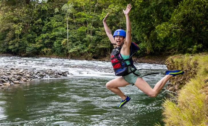 Woman wearing a helmet and life vest jumping into a lake