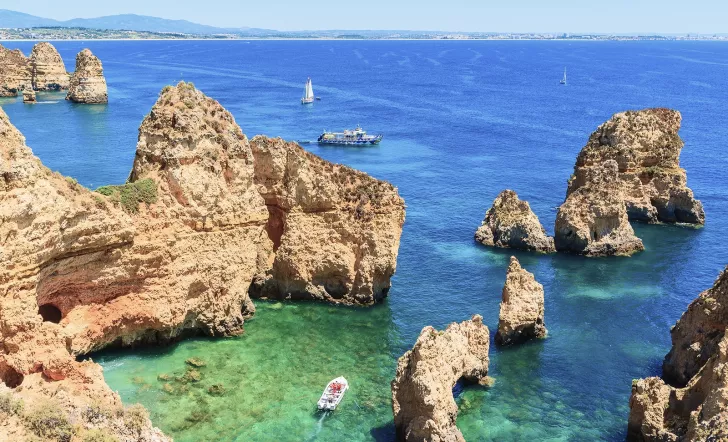 A boat navigating through large cliffs at the edge of the ocean