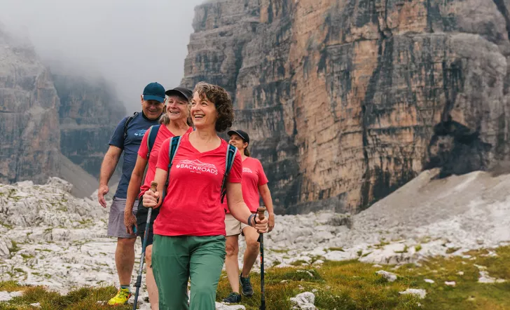 Three women and one man hiking on a grassy trail with fog-covered mountains in the background