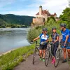 Three bikers walking their bikes on a path along the Danube River.