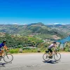 Two bikers riding on a road along the Douro River.