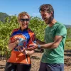 Two bikers posing with a can of wine in a vineyard.