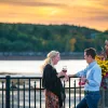 Two guests chatting, wine glasses in hand, sunset and beach in background.